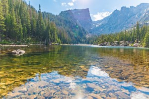 Dream Lake at Rocky Mountain National Park capturing the reflection of Hallett Peak and trees, rocks visible under the clear water of the lake